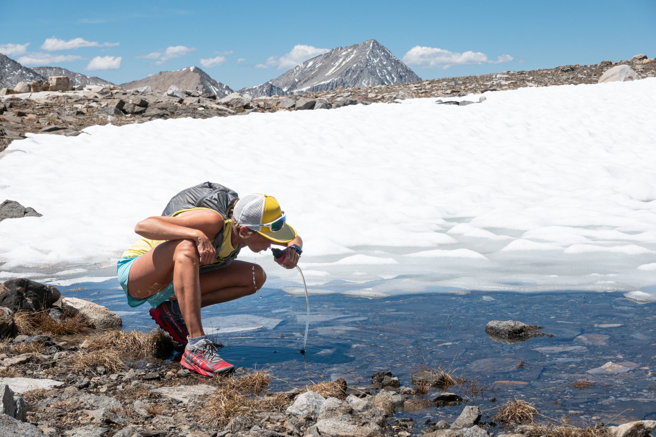 A runner stopped to filter water a small lake while trail running the Taboose Pass Trail to Cardinal Mountain in California's Sierra Nevada