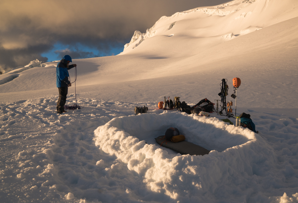 Backcountry camper setting up camp after building natural snow shelter