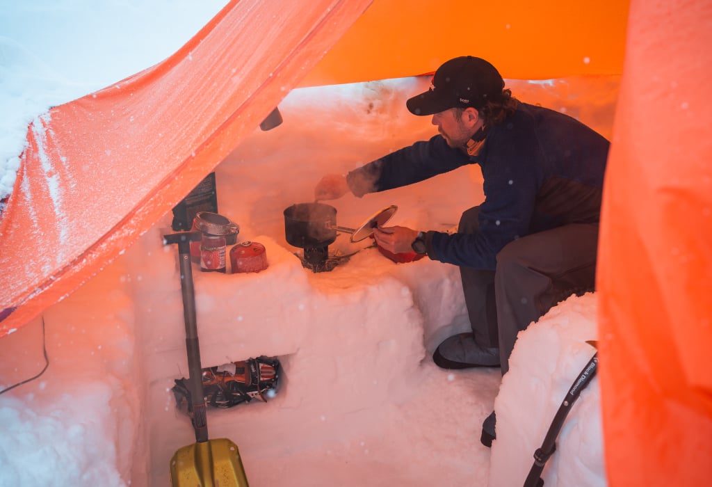 Man cooking dinner in dugout snow trench tent setup