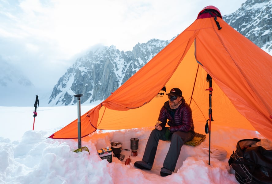 Hiker sitting in MSR Front Range Ultralight Tarp Shelter in snowy mountain