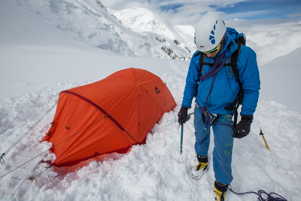 Mountaineer standing next to tent, ready for climbing 