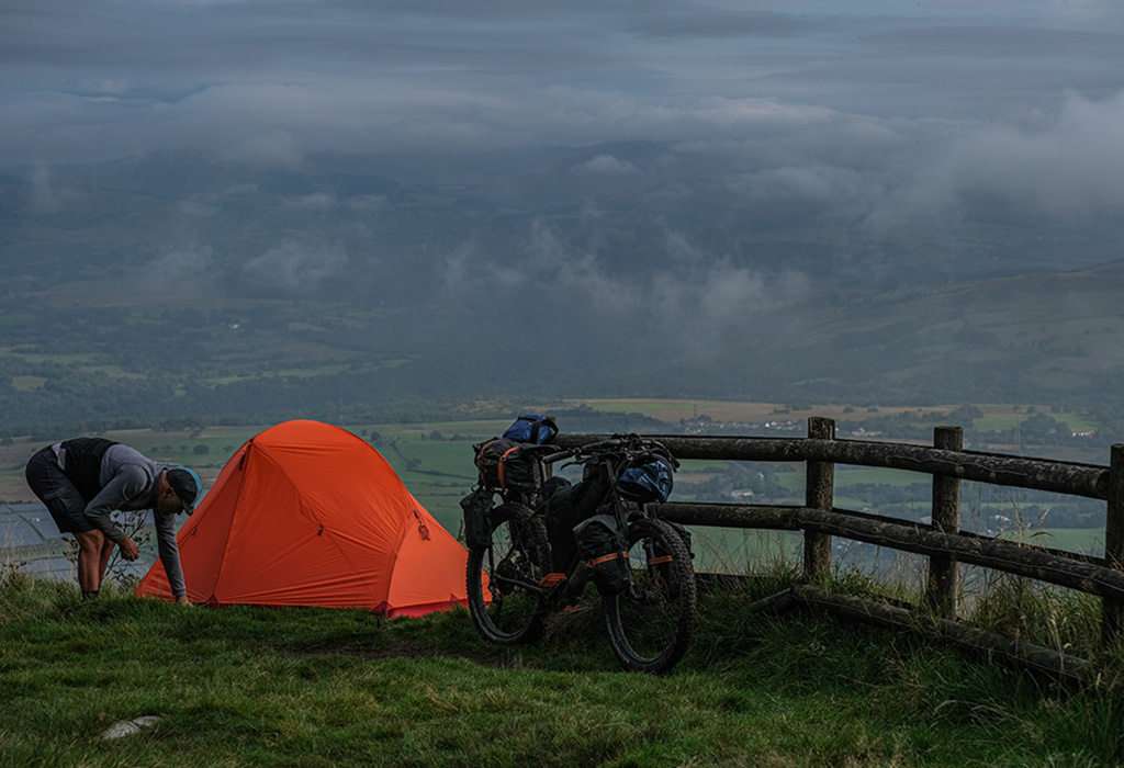 Man setting up bikepacking tent overlooking green valley