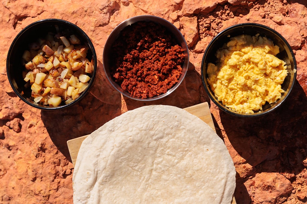 assembling breakfast ingredients on burrito