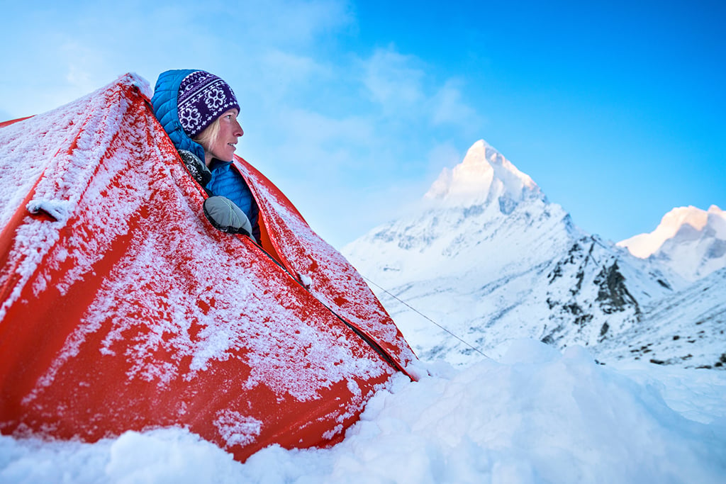 A woman looks out her tent at the fresh snow on the mountain Shivling.